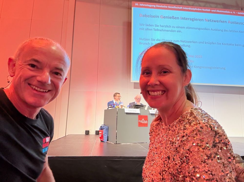 Photo of Nat & Cliff at the DGINA conference with legend Luca Ünlü in the background 