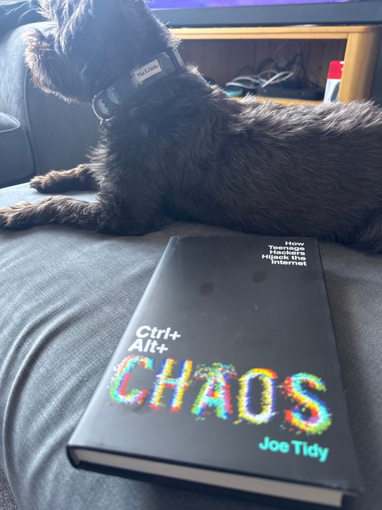 A copy of Ctrl Alt Chaos by Joe Tidy, and a small black YorkiePoo dog. 