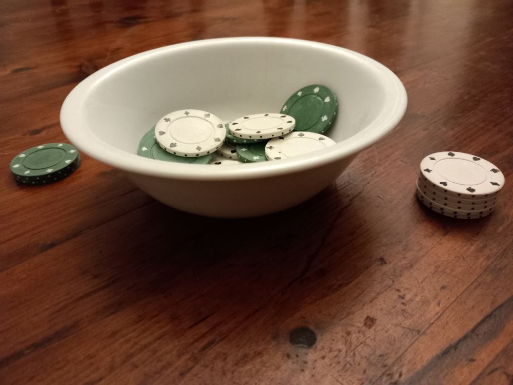 Green and white poker chips in and beside a white bowl on a table. I think I had too much Merlot to explain any reason on why they are there so use your imagination. 