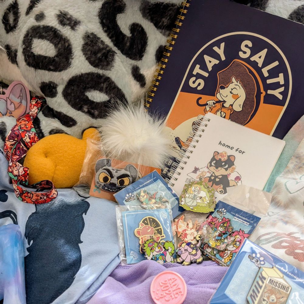 A close-up shot of pins, sticker books, and trinkets received from a furry convention. #ANE #ANE2025 #anthro #furrycommunity