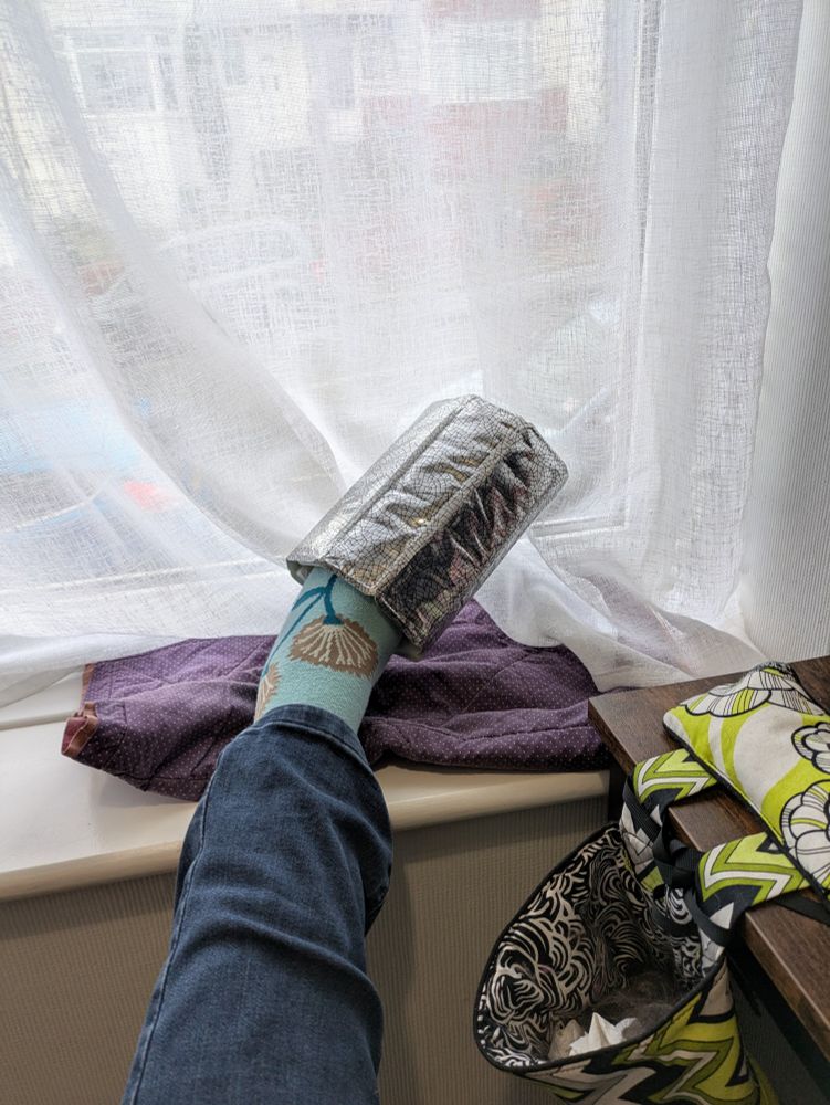Foot in blue flowery socks, with the toes covered by a silver wine chiller collar, propped on a windowsill.