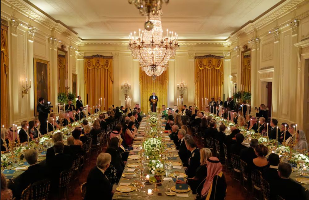 The thoroughly inadequate current ballroom (it clearly needs to be 6 times this size to satisfy the king) at the White House with trump hosting his friends and lots of Saudi Arabian oiligarchs. Nice chandelier, gold drapes (never enough gold, eh?), lots of candles & small floral bouquets.