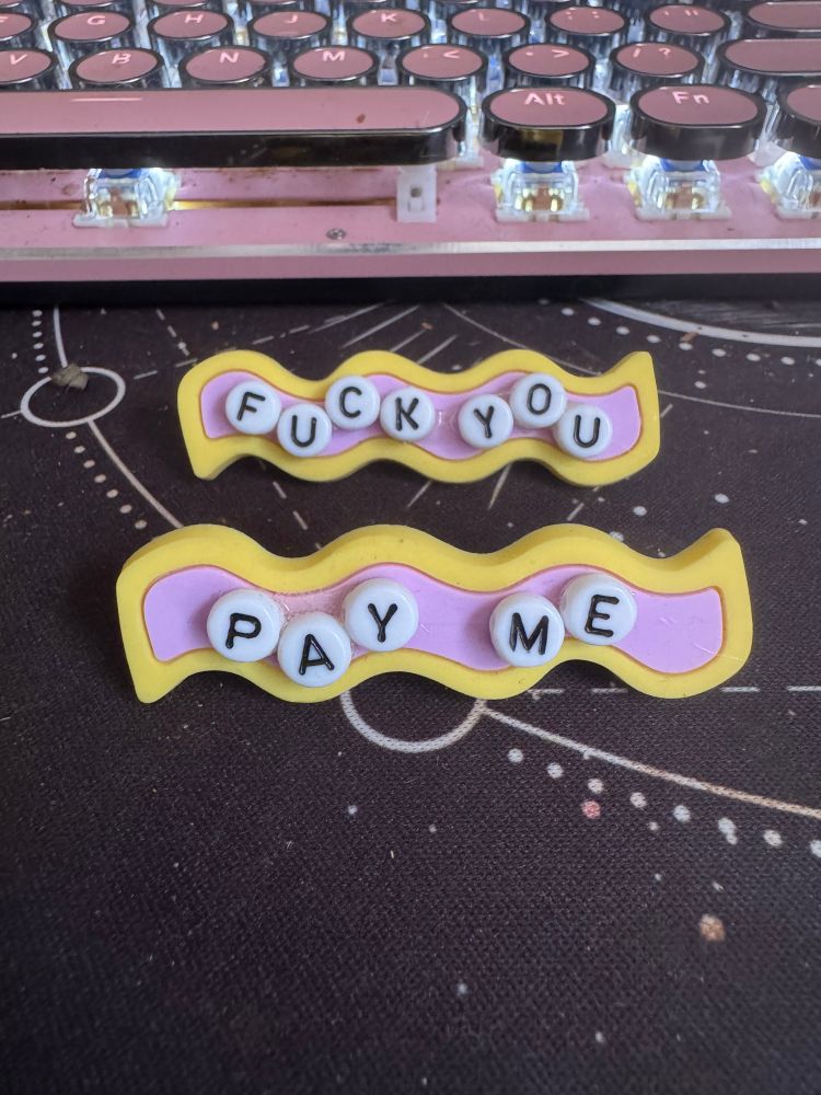 Two clips with the words “fuck you” and “pay me” written in bead letters 