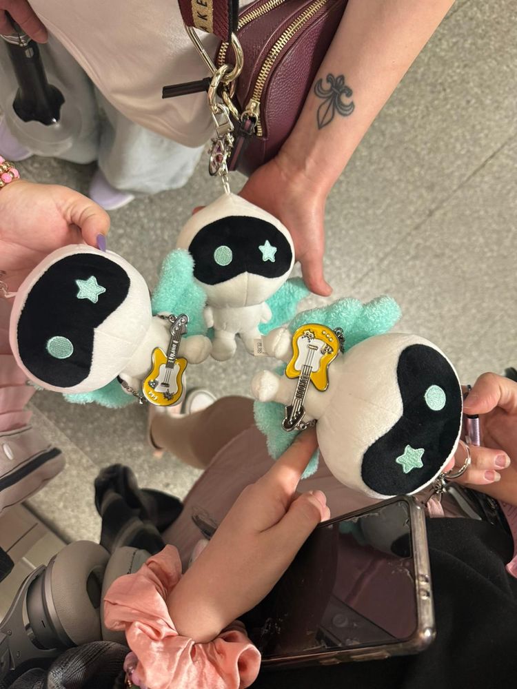 Three Wootteo keyrings in a circle. Two of them are wearing a little yellow guitar from Jin's tour merch for London. 