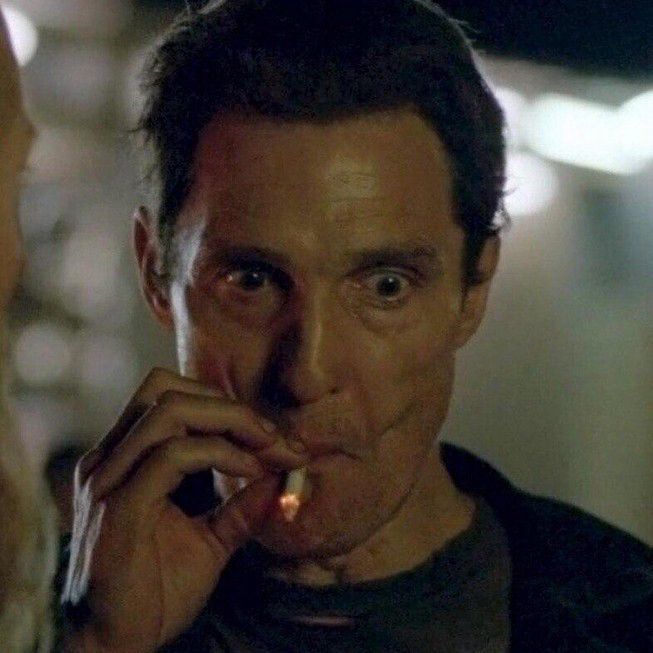 Scene from True Detective season one, Matthew McConaughey smoking and looking at evidence completely caught by the lure of what he is seeing 