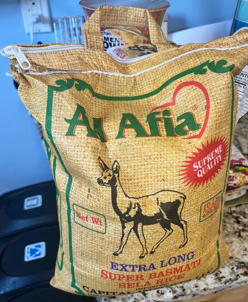 A bag of Al Aida basmati rice. It is in a cloth bag with a sturdy zipper and handles that is screen printed with a deer in it and to look burlap. The design is mostly green with some red, black, and blue elements.