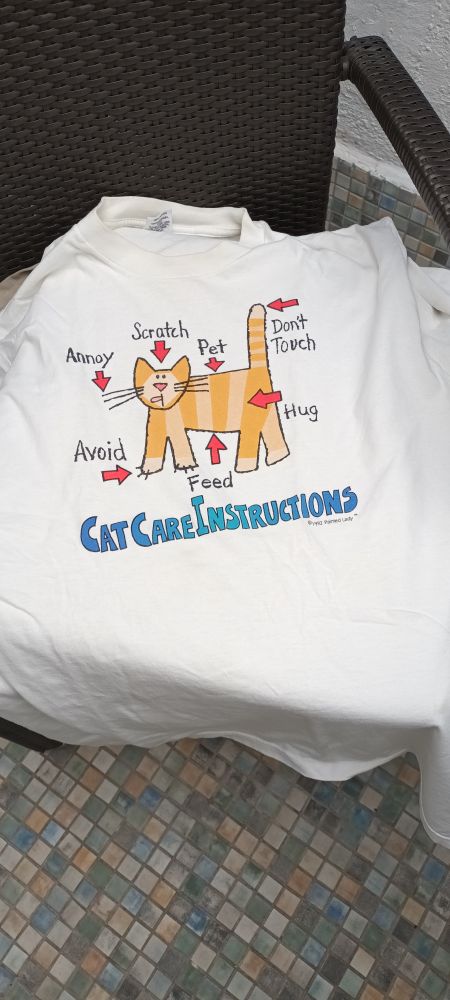 A T-shirt with the picture of a ginger cat and care instructions: hug (body), pet (back), scratch (head), annoy (whiskers), feed (belly), avoid (claws), don't touch (tail). 