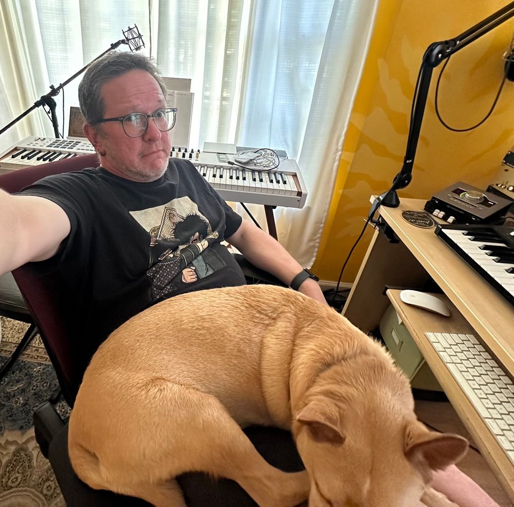 Mark sits in his chair, pinned down by Freddie (a brown dog) who jumped in his lap and fell asleep in a 90-second window.