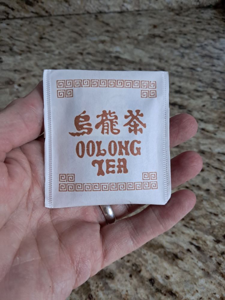 Mão de mulher branca segurando um sachê de chá oolong 