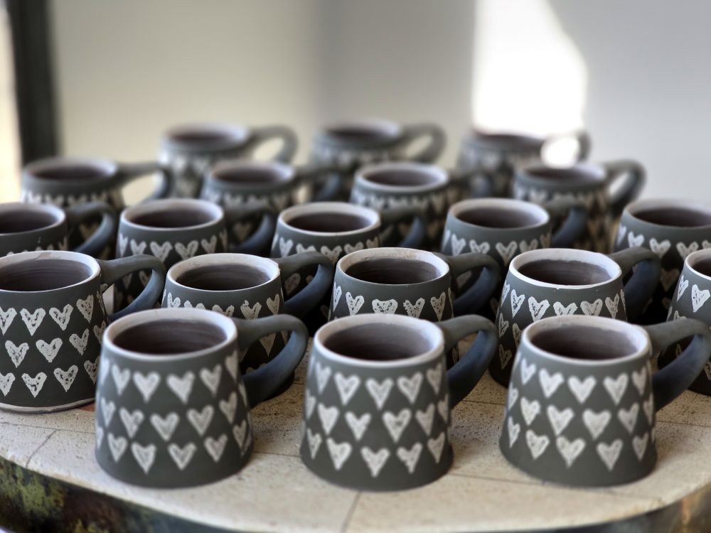 White patterned heart mugs with a black background drying on top of a warming kiln.