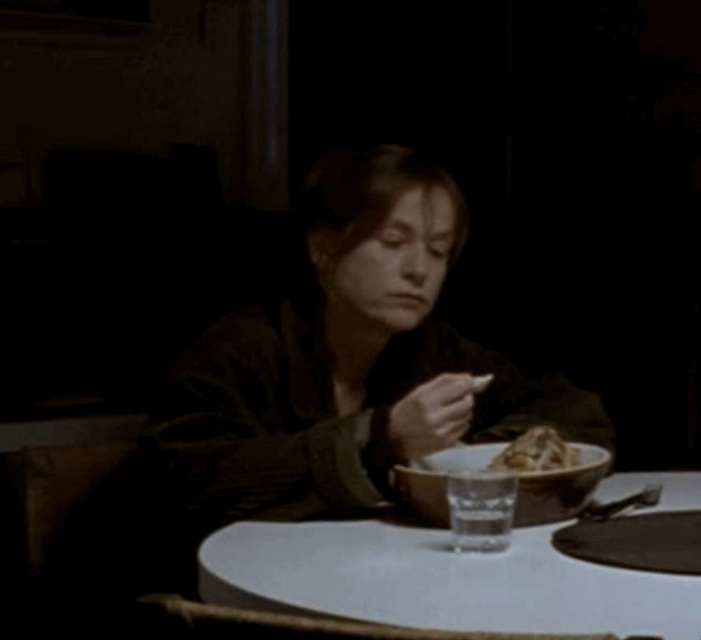 a woman sits at a table with a bowl of food and a glass of water in front of her