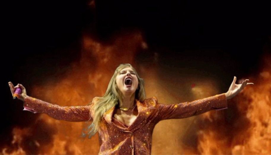 edited photo of taylor swift during the man at the eras tour. she’s wearing the ORANGE!!!! blazer, has her arms opened wide and is looking up and yelling. there is fire edited behind her 