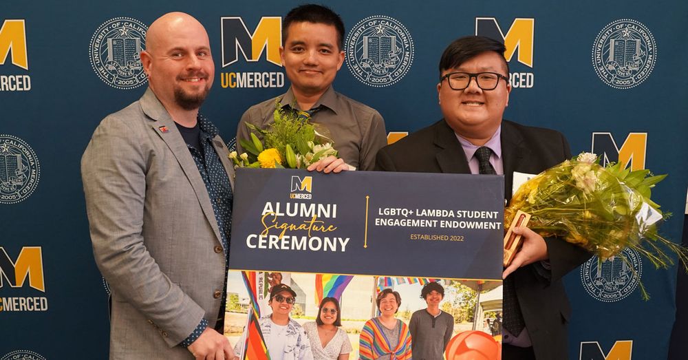 Alumni Keith Ellis, Derek Sollberger, and Jonathan Ly pictured together holding bouquets of flowers and signage highlighting the LBGTQ+ Lambda Student Engagement Endowment.