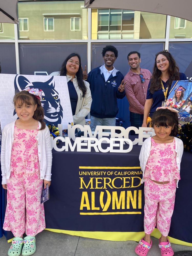 Two young future Bobcats pose in front of the alumni table with four UC Merced alumni. Photographed by fellow alumna, Lourdes Miranda '15.