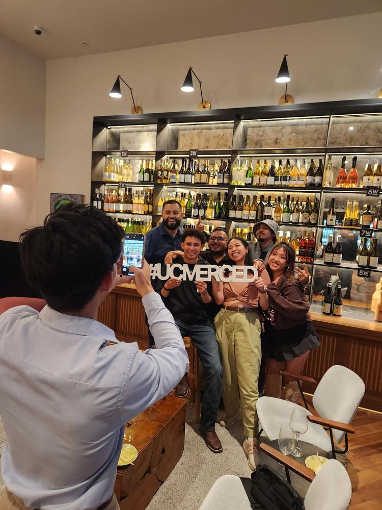 An alum captures a group photo of alumni and friends as they proudly pose with a #UCMerced sign.