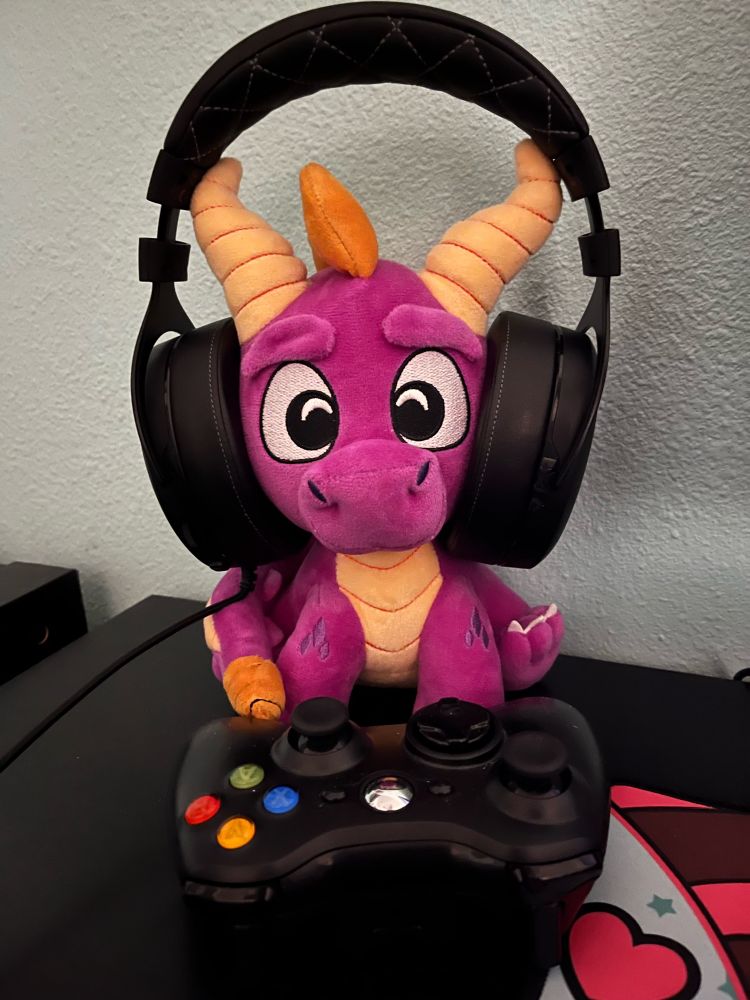 A spyro plushie with headphones on in front of an Xbox 360 controller
