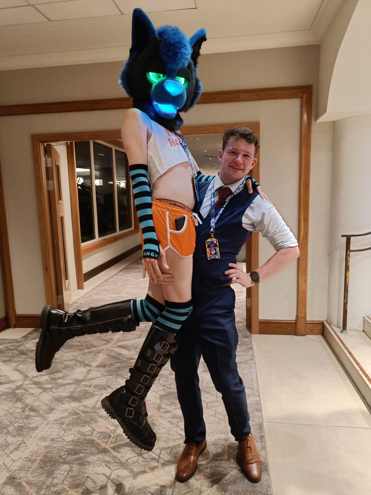 Huxley wearing a suit lifting Dan The Glow Wolf dressed as a femboy hooter