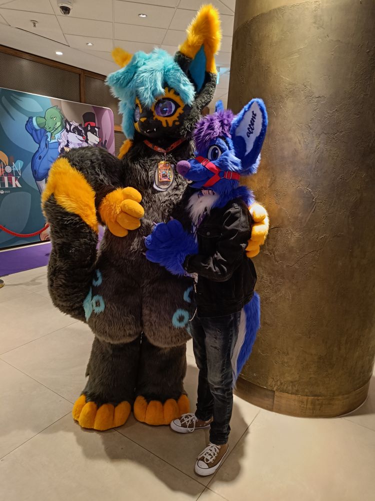 Two fursuiters, Keevy and Accent, posing beside each other in a hug