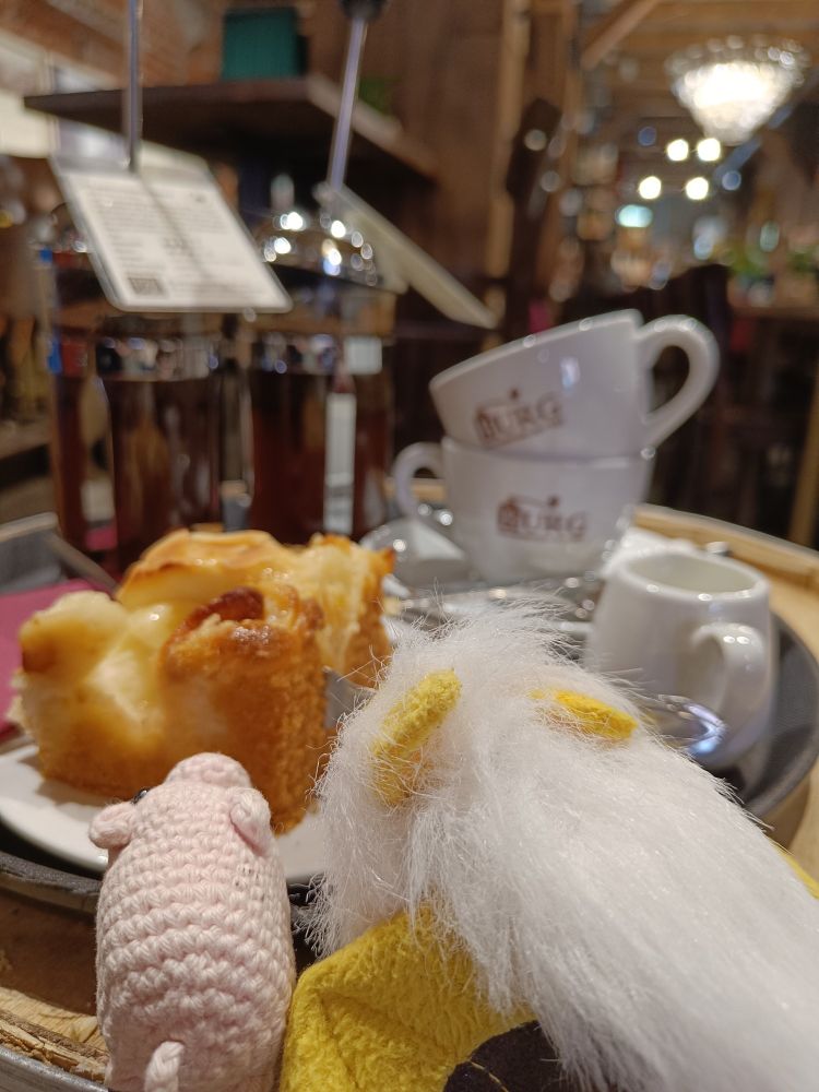 a small bat and piggy plushie looking at a piece of Apfelkuchen and coffee cups