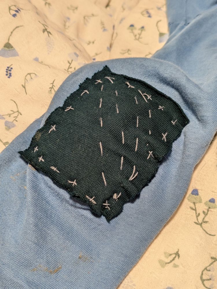A dark blue patch sewed onto a blue sleeve with silver thread.