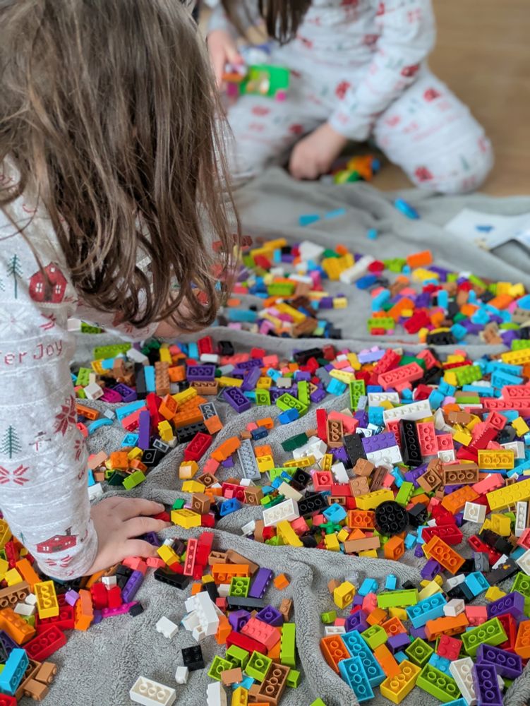 Two young kids playing on a blanket filled with colourful legos.