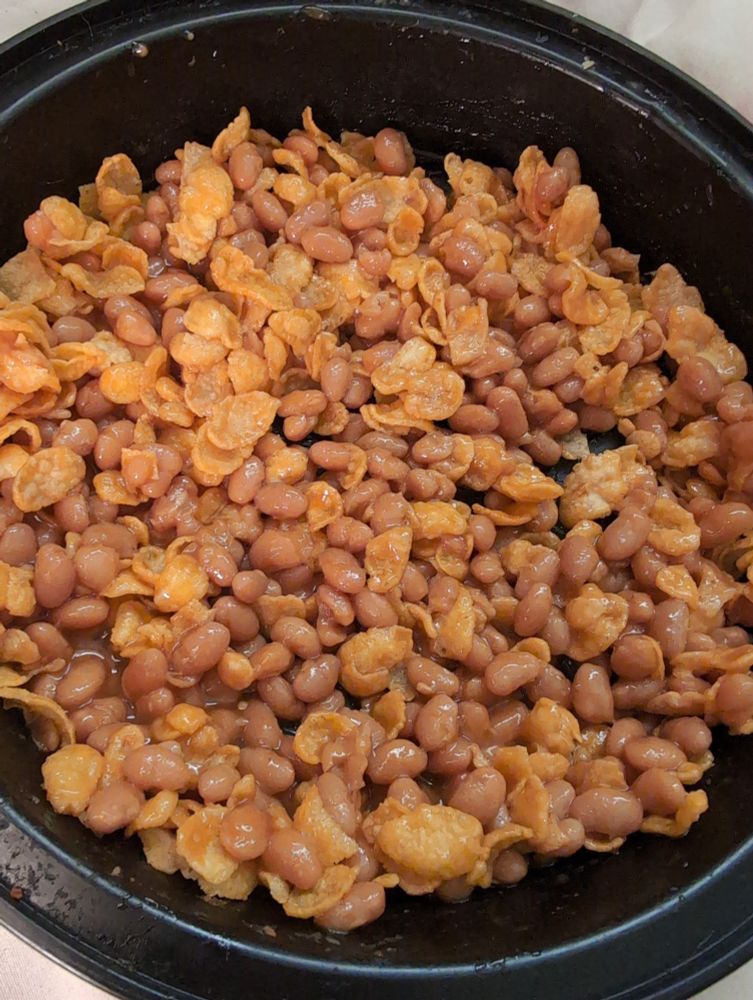 A black bowl filled with baked beans and cornflakes.