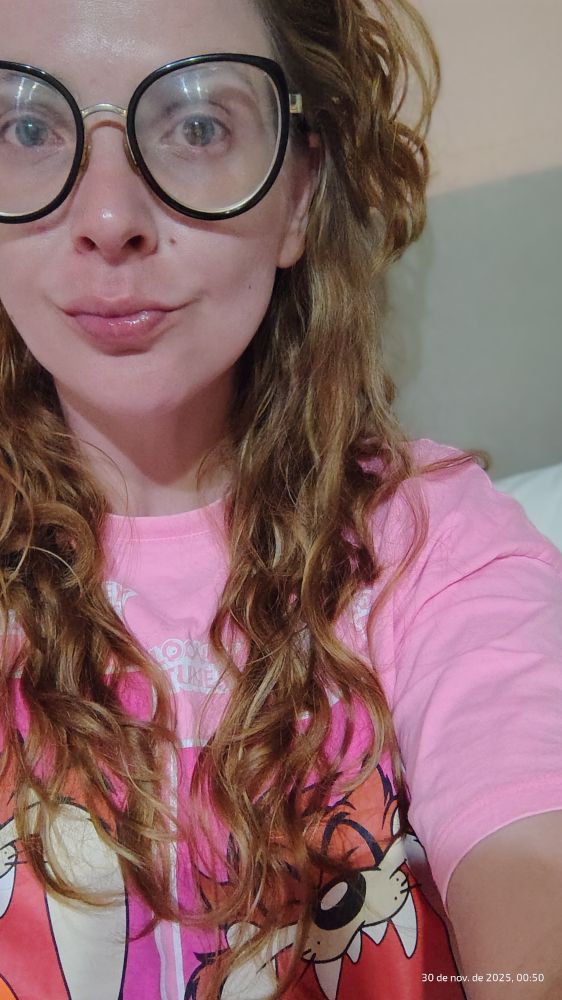 série mulher branca de cabelo castanho claro ondulado e comprido, de óculos de grau e camiseta rosa