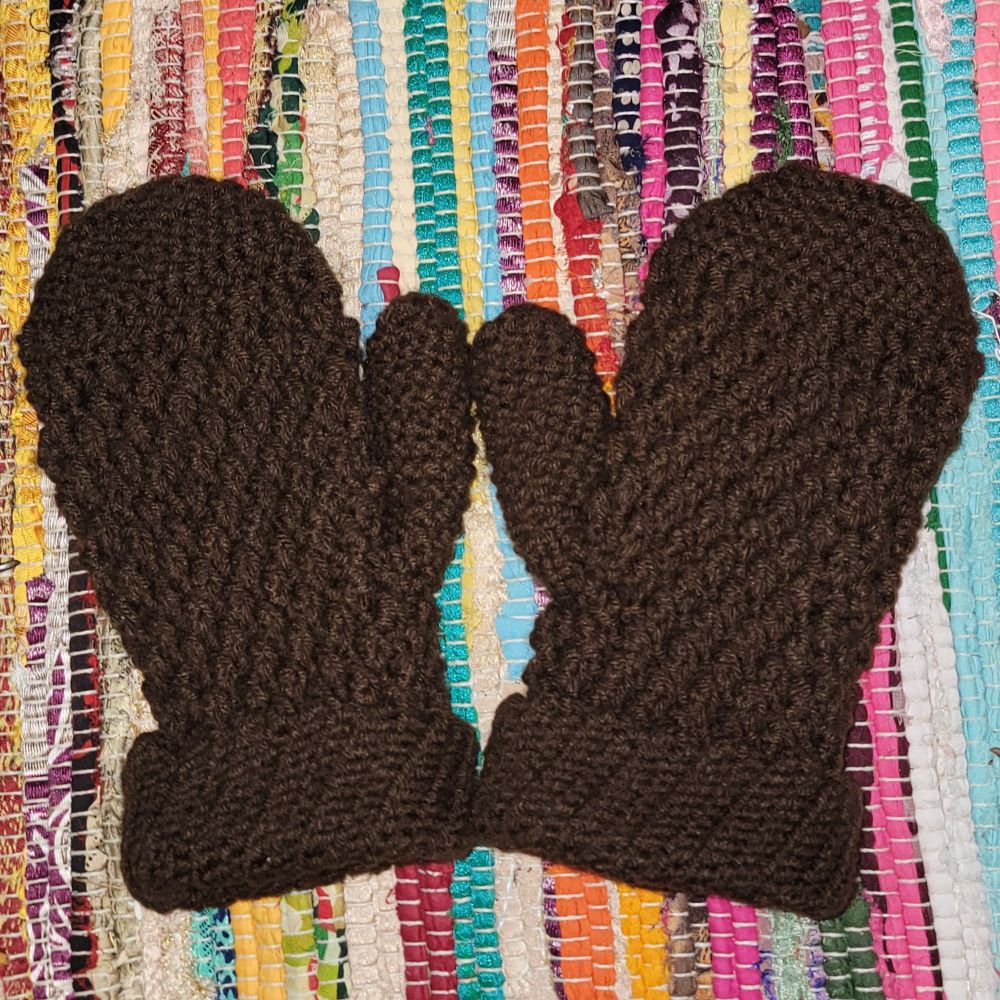Two brown crochet mittens on a rainbow recycled fabric rug 