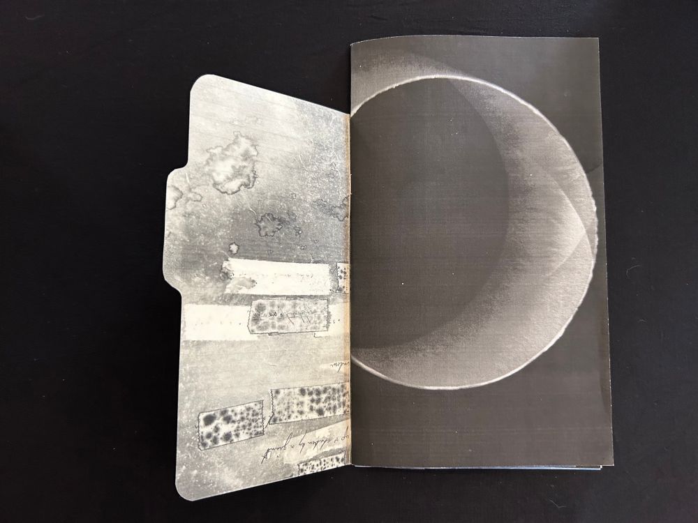 Artist’s book with the image showing the inside cover made of a file folder and the opposing page showing a half-round photogrammed form resembling a crescent moon.