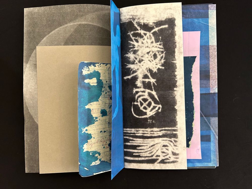 The book displayed opened to its center with papers of various sizes visible. The pages are beige, blue and pink and have been printed with abstract forms, with hints of nearly legible texts appearing. 