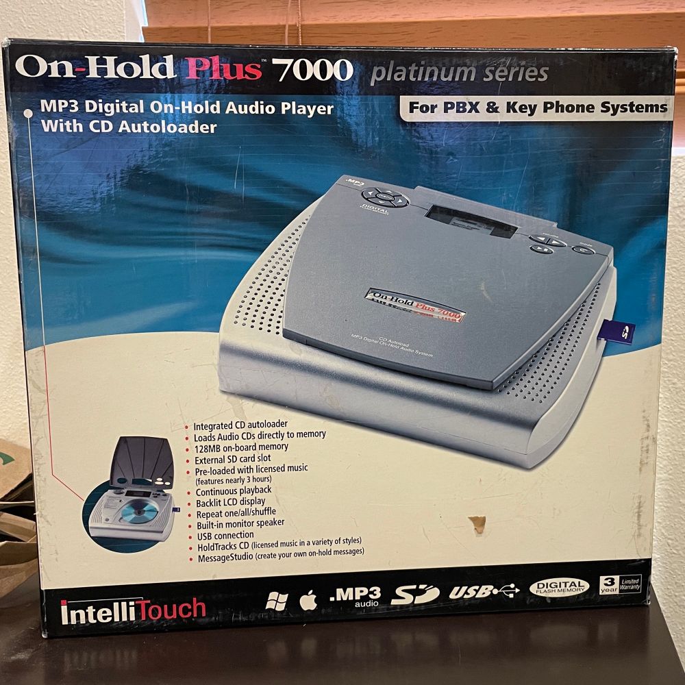 Photo of a cardboard box for a "On-Hold Plus 7000 MP3 Digital On-Hold Audio Player with CD Autoloader." The box is yellowed and faded with age.