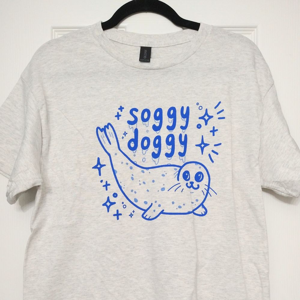 gray shirt printed with blue ink graphic of a seal with its tail lifted in the air with text "soggy doggy"