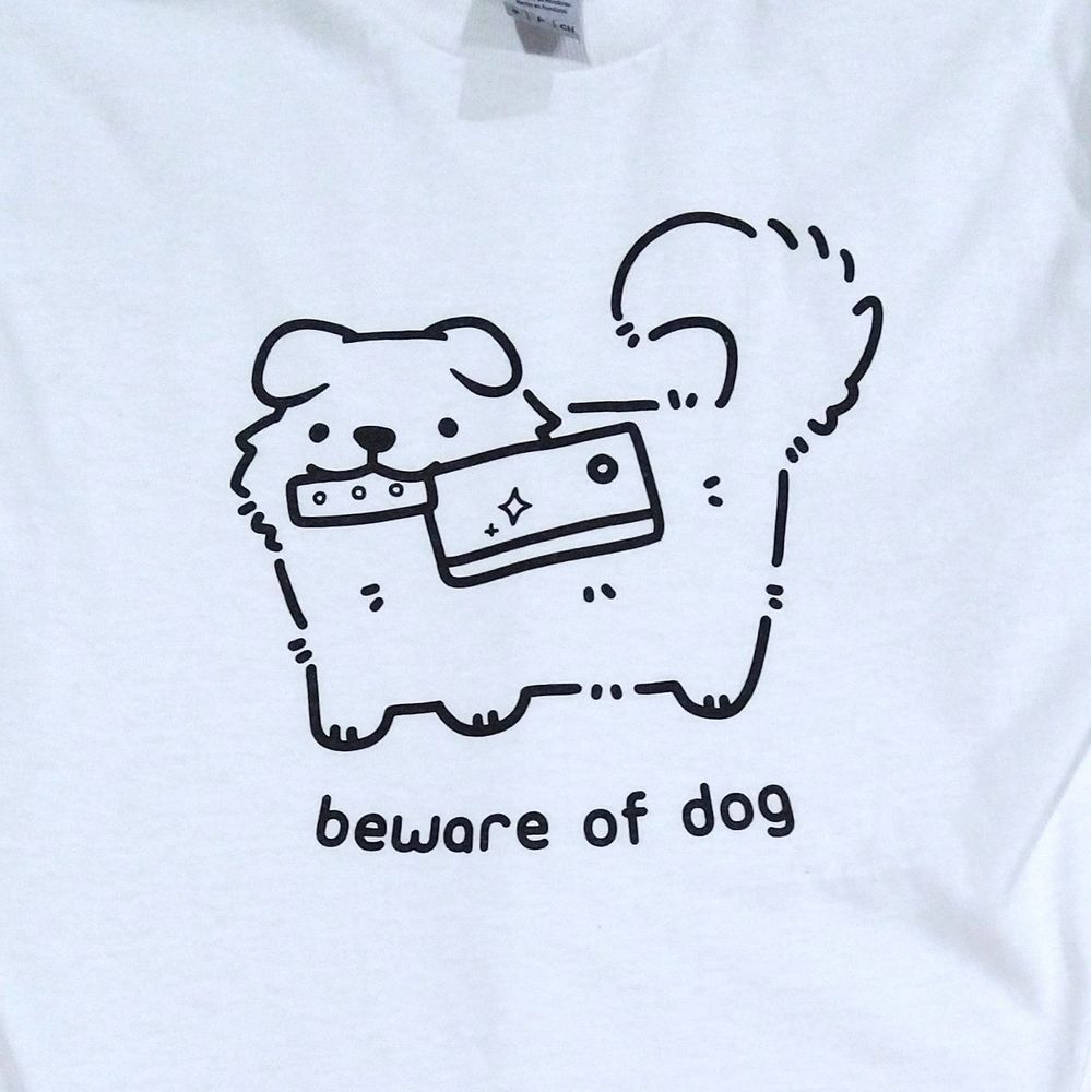white shirt with drawing of a cute dog holding a kitchen cleaver in its mouth. text "beware of dog"