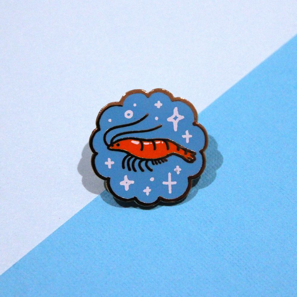 enamel pin of a shrimp with a blue background and sparkles