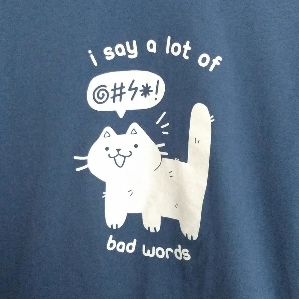 blue tee printed with white graphic of a cat drawn in a cute style saying cartoonishly censored symbols. text reads "i say a lot of bad words"