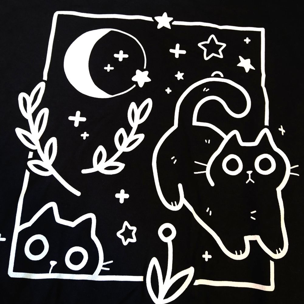 Black tee printed with cats, plants, moon and stars in white ink