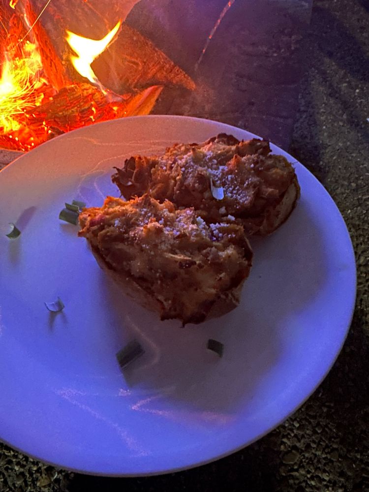 A while corelle dinner plate with 2
Halves of a stuffed baked sweet potato. You can’t make out the colors as it’s dark but you can see the fire in the background 