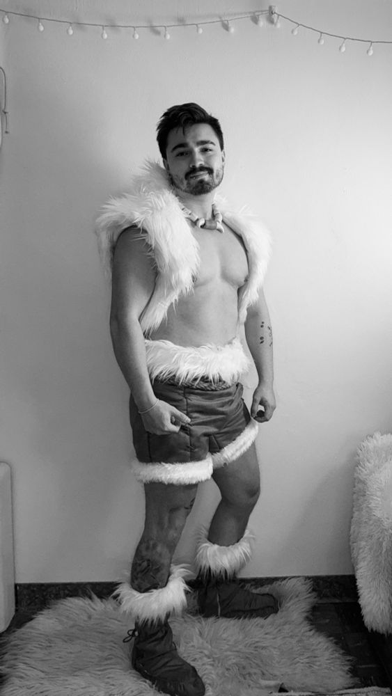Black and white 3/4 angle of me in front of a white wall and standing on a sheep skin. I’m wearing made handmade nuktuk costume.