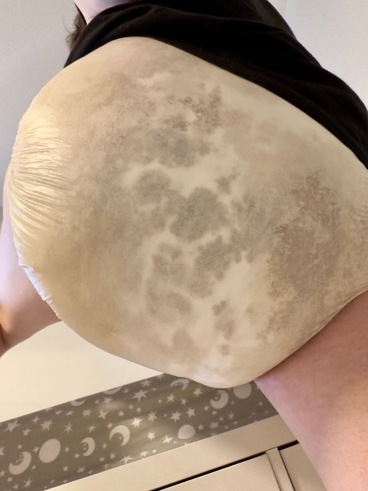 Close up of the rear and bottom of someone wearing a diaper. The diaper was once white but has been so heavily used and stained that it is now various shades of brown and yellow, with mucky cloudy patches of darker brown mixed in.