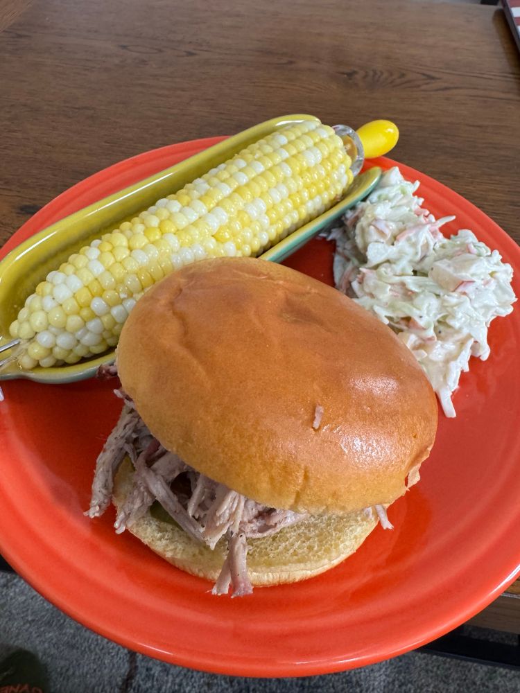 A plate full of food including a helping of coleslaw, corn on the cob, and a pulled pork sandwich.