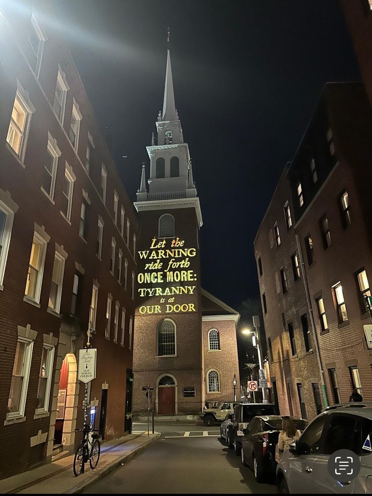 Photo of the old North Church at night in Boston on the 250th anniversary of the midnight ride of Paul Revere displaying "Let the warning ride forth once more: Tyranny is at our door" on it's face by light projection.