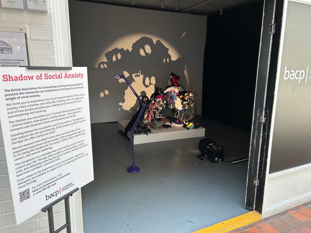 Shadow of Social Anxiety campaign and sign. This is an immersive art installation featuring a sculpture made up of everyday items that represent social situations where people may feel social anxiety. The shadow represents the feeling of isolation of people struggling with social anxiety and the fear that people are judging them. 