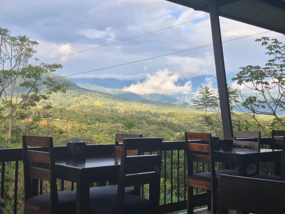 A view from a balcony of a valley with mountains and clouds. 