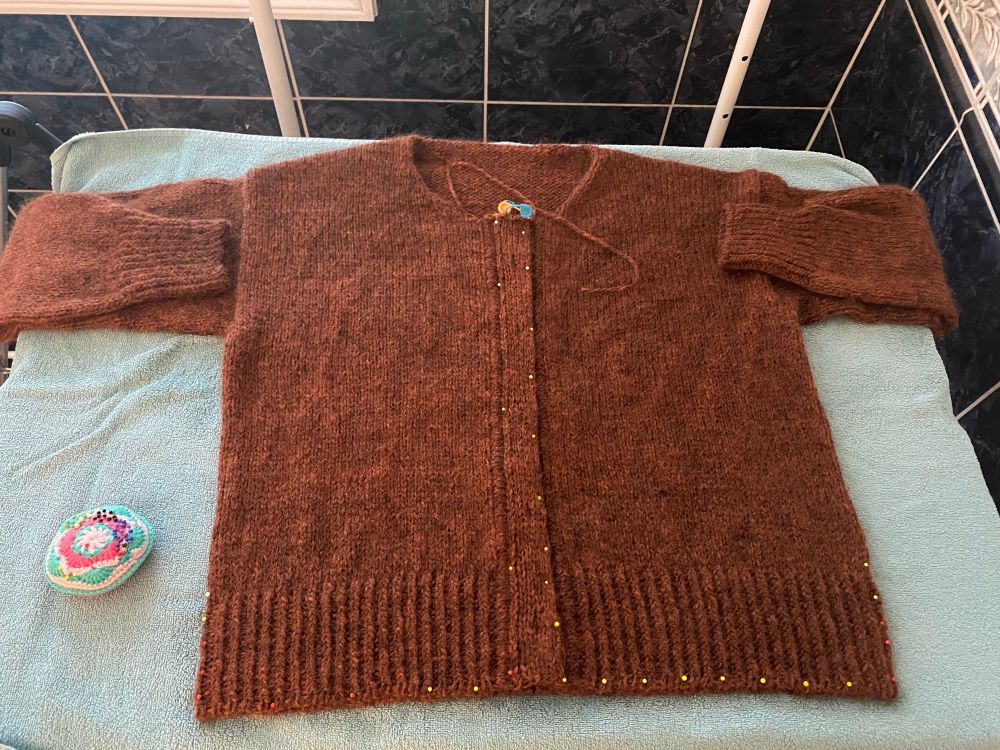 an orange brown knit cardigan laid on a towel and blocking mat. it’s been pinned down with a million pins. it looks super straight and flat