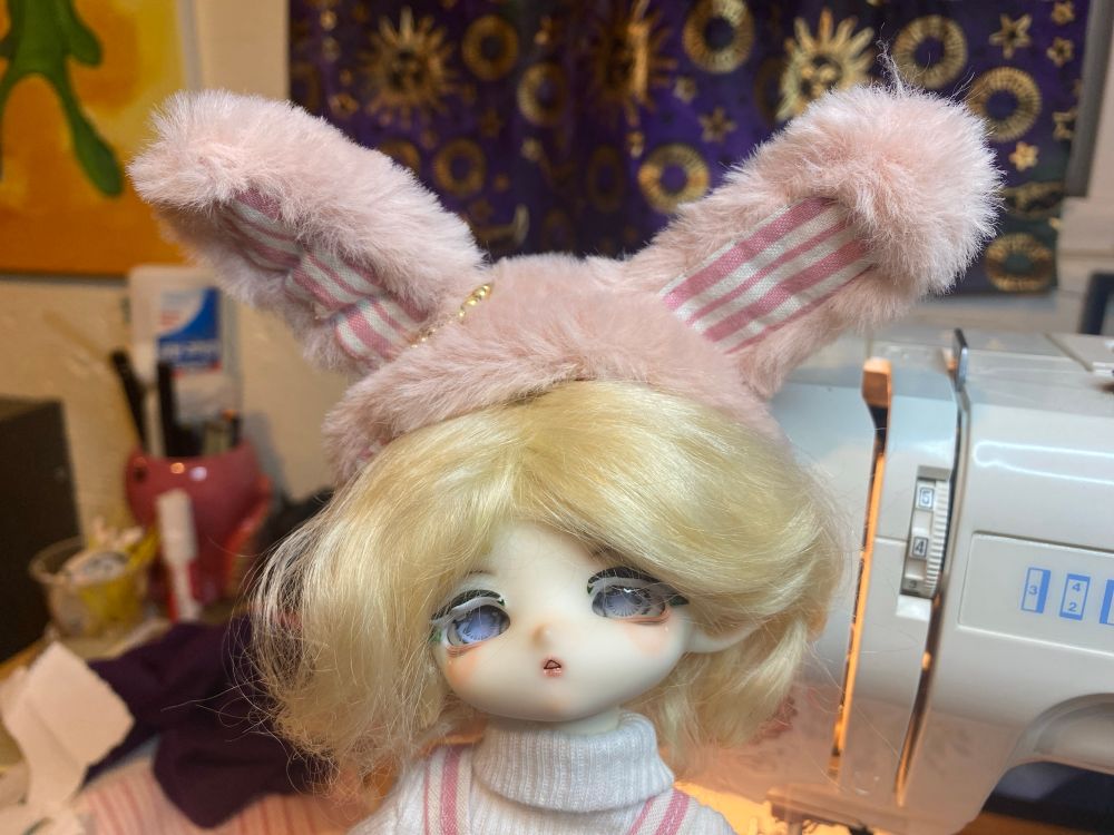 A close-up of a Whale Island Crocodile Bobby doll wearing a custom-made outfit including a matching rabbit hat.