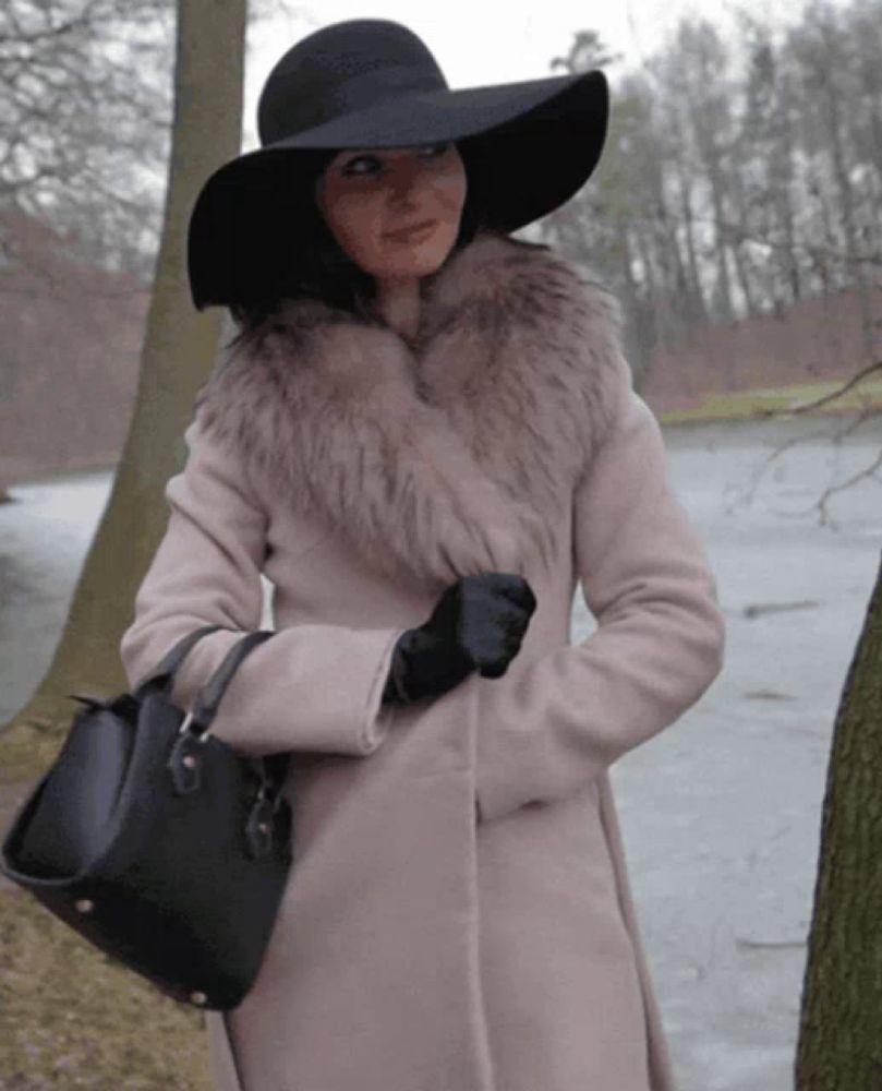 a woman wearing a black hat and a white coat is holding a black purse