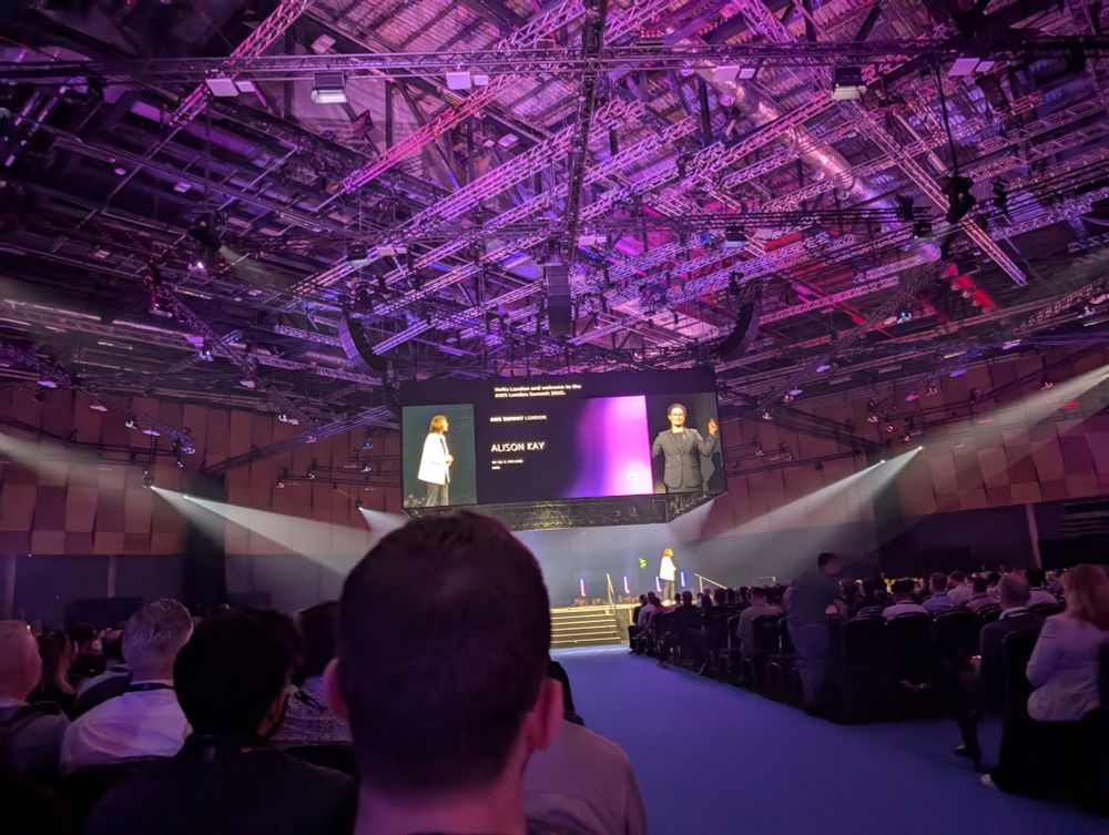 A conference keynote with a screen displaying the slides, captions, and sign language interpreter on screen