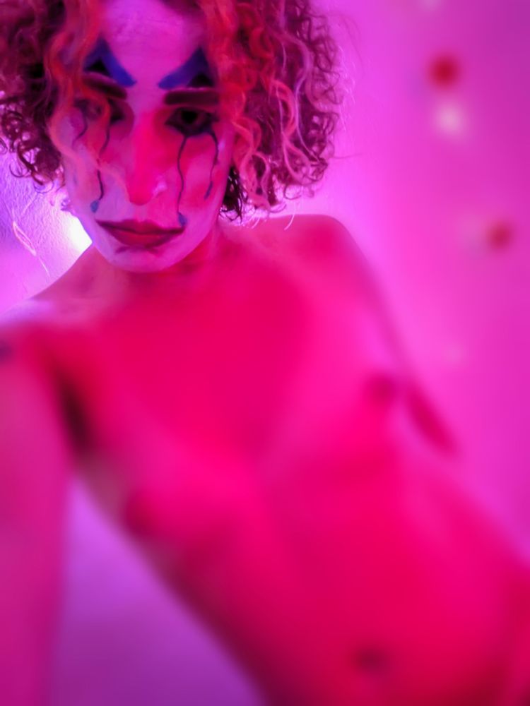 Broken hearted clown stares at you through a daze as light illuminates her from behind