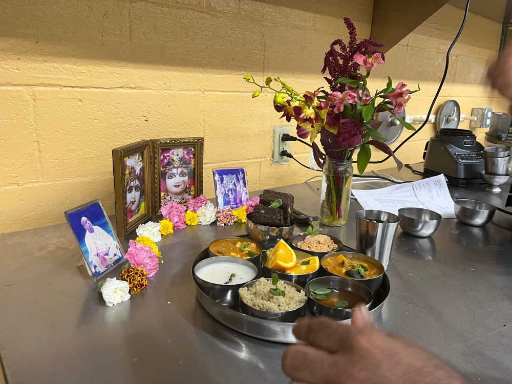 A plate of food (rice, chutney, curry, cream) being offered at a small Hare Krishna altar. 