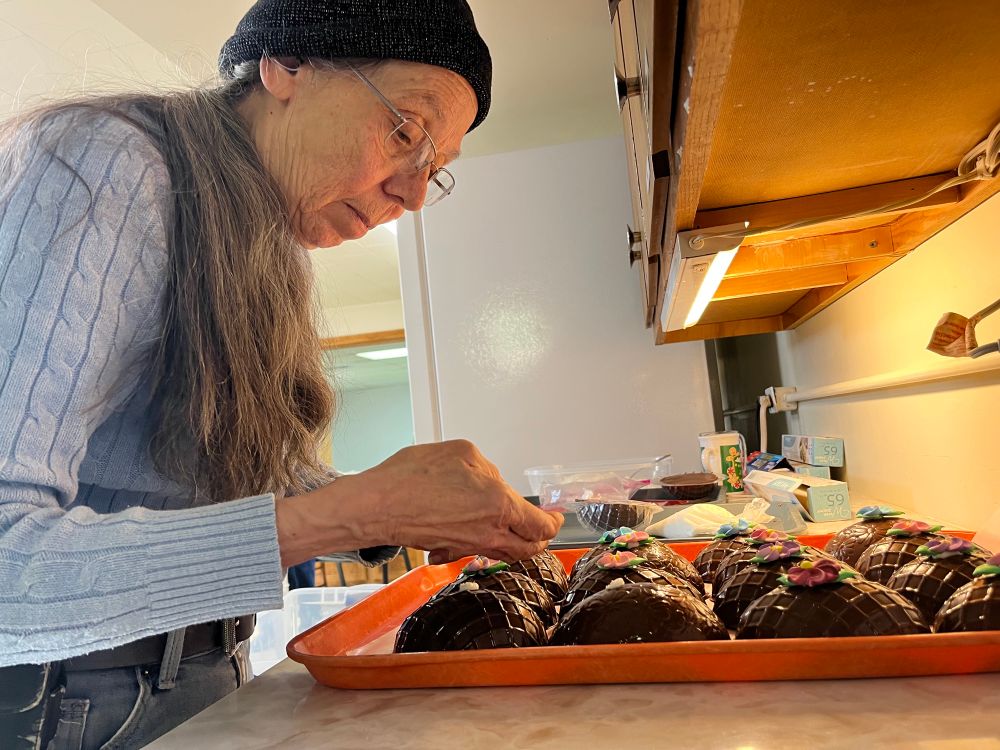 A woman decorated chocolate eggs with small sugar flowers.